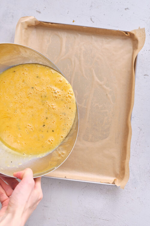 Egg wash being poured into a baking pan lined with parchment paper for baking or cooking.
