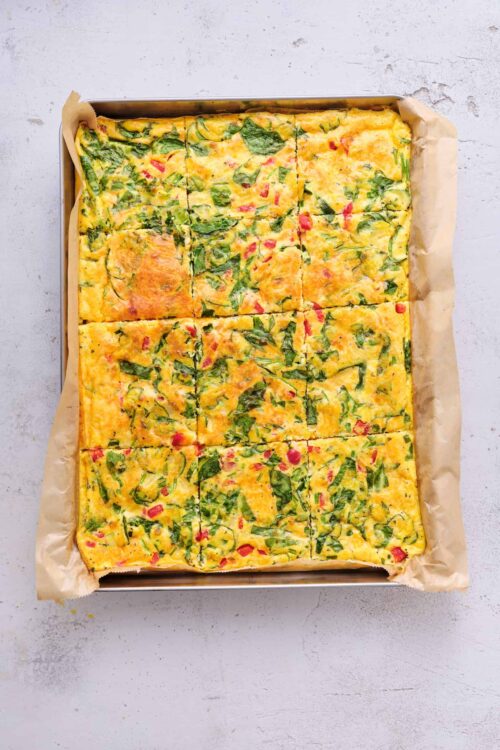 Cheese and vegetable breakfast casserole with spinach and red peppers on parchment paper.