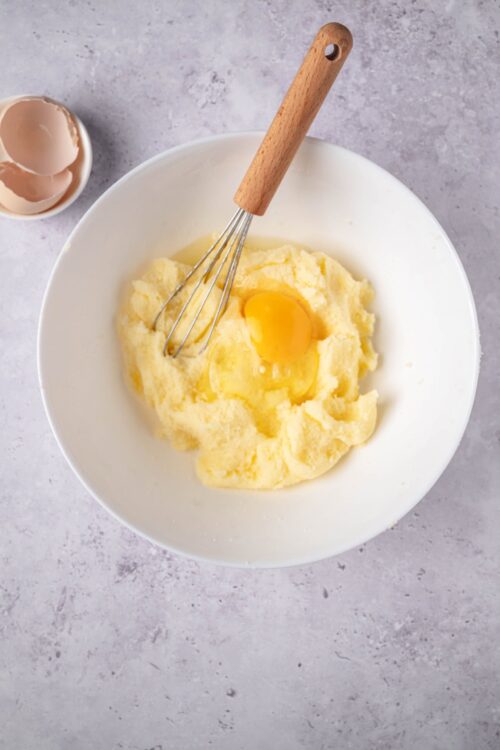 Creamy mashed potatoes with a raw egg in a white bowl on grey background.