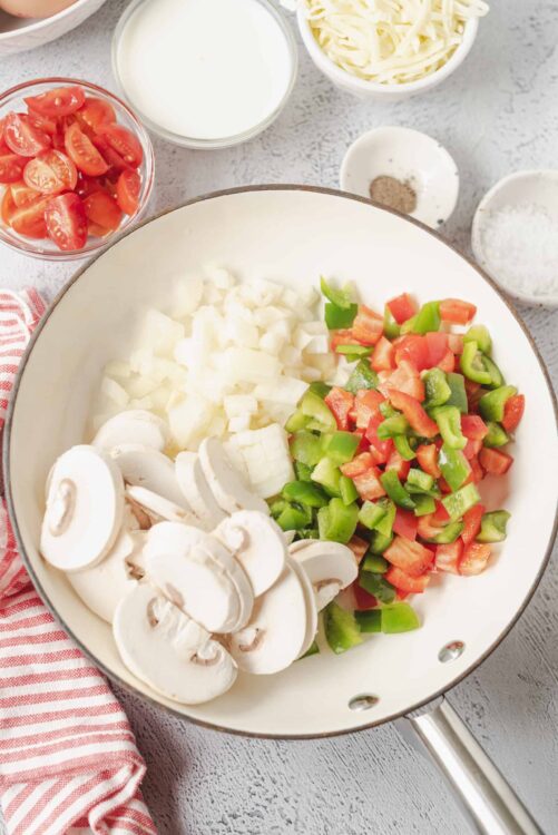 Chopped vegetables and ingredients for pizza in a white skillet, including mushrooms, onions, and bell peppers.