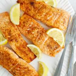 Juicy baked salmon fillets with lemon wedges on a white plate, perfect for healthy dinner recipes.