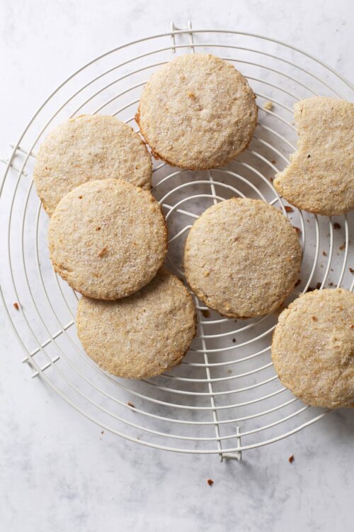 Buttery sugar cookies on a cooling rack with a bite taken out.