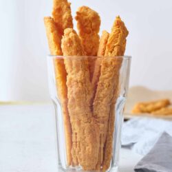 Golden fried chicken tenders in a tall glass.