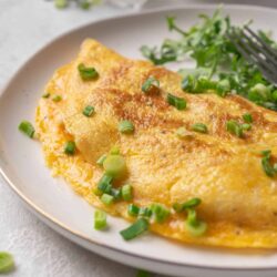 Fluffy cheddar cheese omelette garnished with green onions on a white plate.
