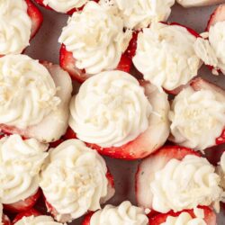 Fresh strawberry bites topped with creamy whipped cream and white chocolate shavings, a delightful summer treat.