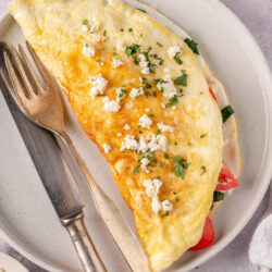 Fluffy omelette with fresh herbs, cheese, and vegetables on a white plate.