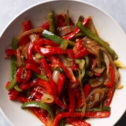 Sautéed colorful bell peppers and onions in a white bowl, fresh vegetable stir-fry.