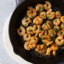 Juicy garlic butter shrimp sautéed in a cast-iron skillet garnished with fresh parsley for a easy seafood recipe.