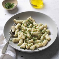 Buttered gnocchi garnished with chopped parsley on a white plate.