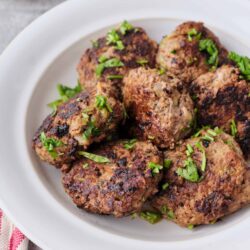 Juicy homemade beef meatballs garnished with fresh herbs on a white plate.