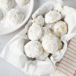 Flour-dusted lemon infused snowball cookies in a white paper-lined basket.