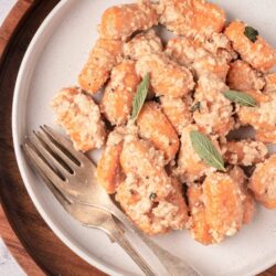 Sweet potato gnocchi with sage leaves on a white plate, rustic serving dish.