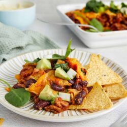 Savory beef chili with black beans, topped with fresh avocado on a white plate.