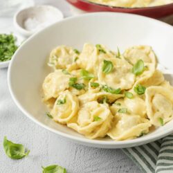 Creamy cheese tortellini with basil in a white bowl, homemade pasta dish from Baked Bree.
