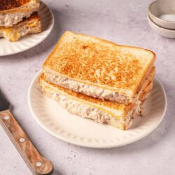 Golden brown grilled cheese sandwich with creamy filling on a white plate.