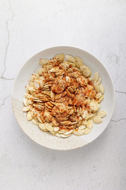 Roasted pumpkin seeds in a white bowl, seasoned with spices for healthy snacking.