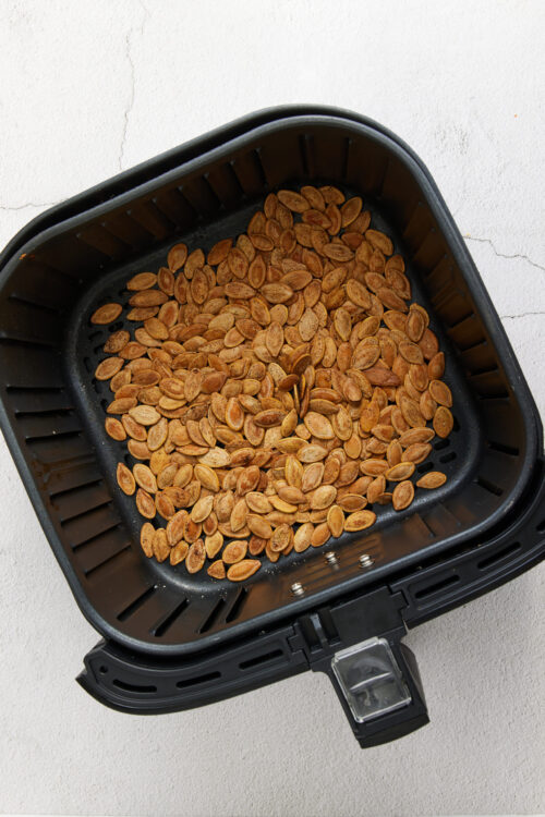 Roasted pumpkin seeds in an air fryer on a white surface.