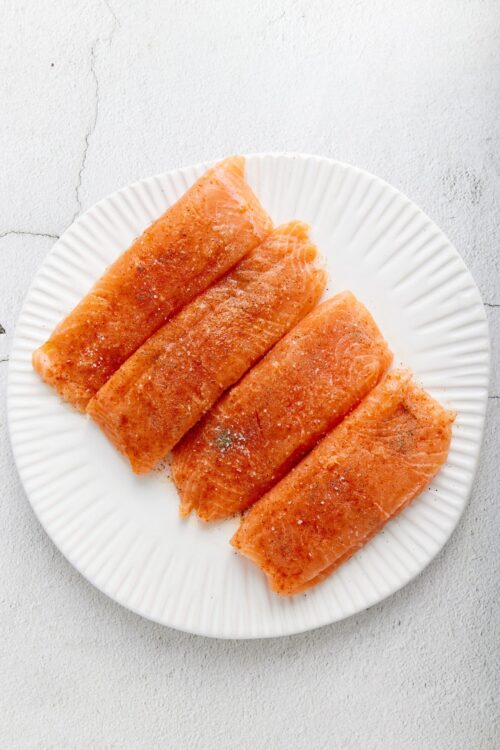 Salmon fillets seasoned with salt and pepper on white platter.