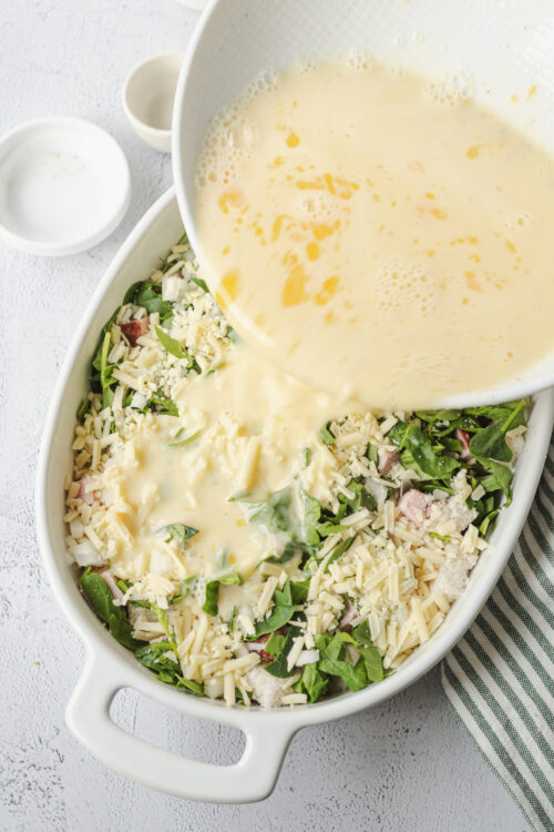 Creamy cheese sauce being poured over fresh vegetable casserole for baked cheese broccoli dish.