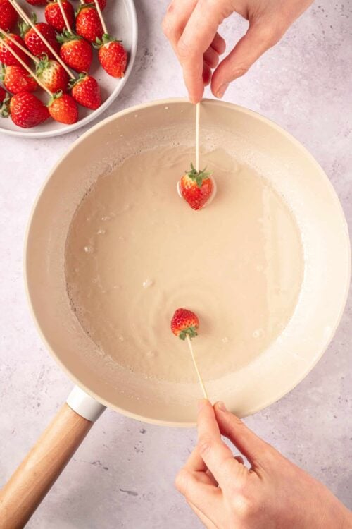 Fresh strawberries on skewers being dipped in white chocolate in a bowl, perfect for strawberry chocolate skewers or desserts.