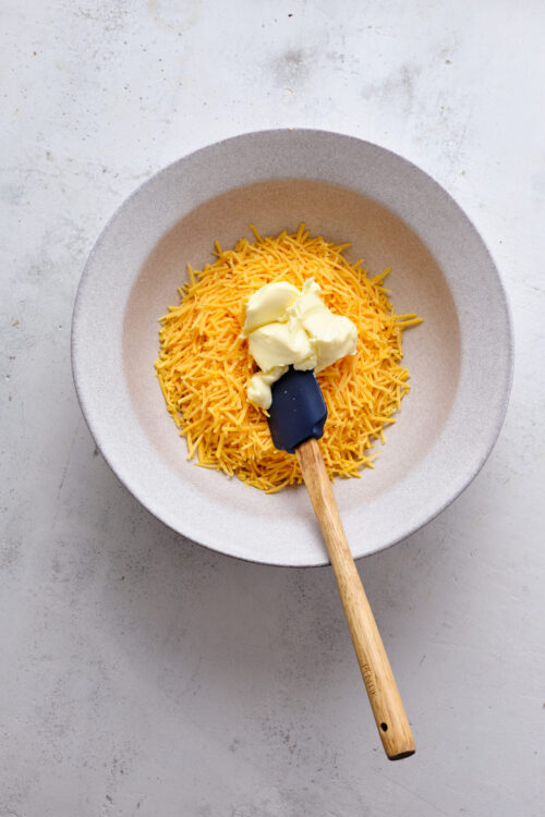 Shredded cheddar cheese and cream cheese in a white bowl for baking recipes.