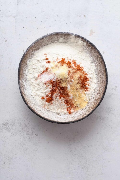 Flour, spices, and baking ingredients in a mixing bowl for baked good recipes.