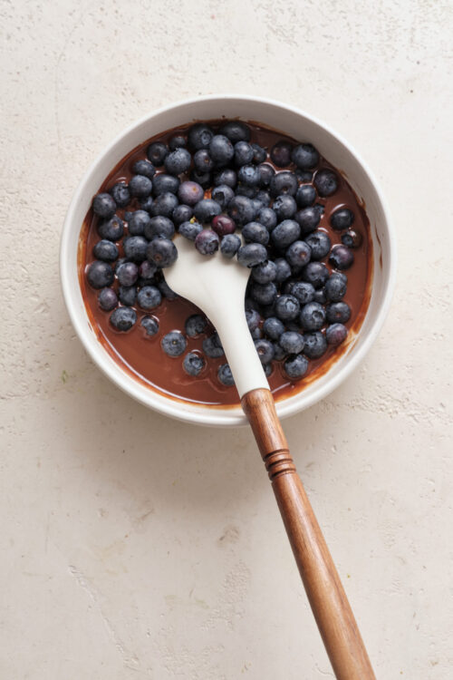 Fresh blueberries on chocolate pudding in a white bowl with a wooden-handled spoon.
