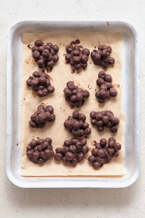 Chocolate cluster candies on parchment paper in a baking dish, ready for cooling.