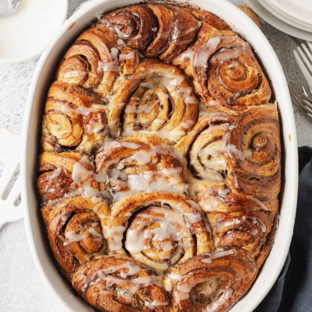 Buttery cinnamon rolls with white glaze icing in a baking dish.