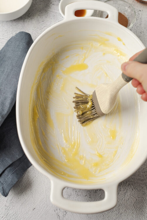 Creamy butter and egg mixture being spread in a white ceramic baking dish for cooking or baking.