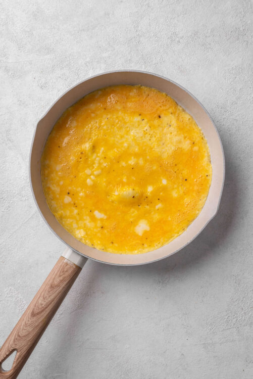 Fluffy scrambled eggs cooking in a non-stick skillet with a wooden handle.
