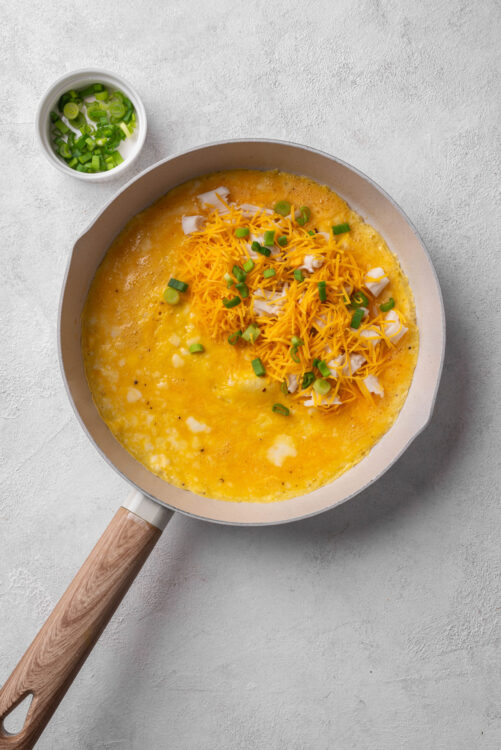 Creamy scrambled eggs with shredded cheddar cheese and chopped green onions in a skillet.