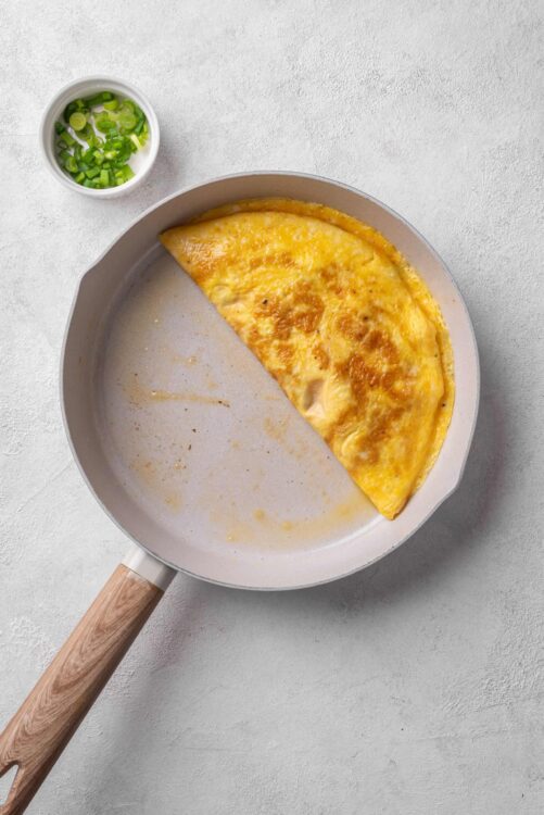 Scrambled eggs in a skillet with chopped green onions on a white surface.