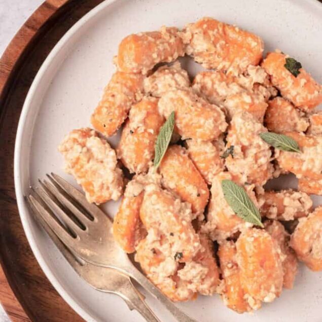 Golden roasted sweet potatoes with fresh sage leaves, served on a white plate for a delicious side dish.