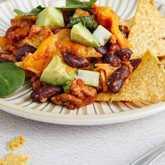 Savory beef chili with black beans, topped with fresh avocado on a white plate.