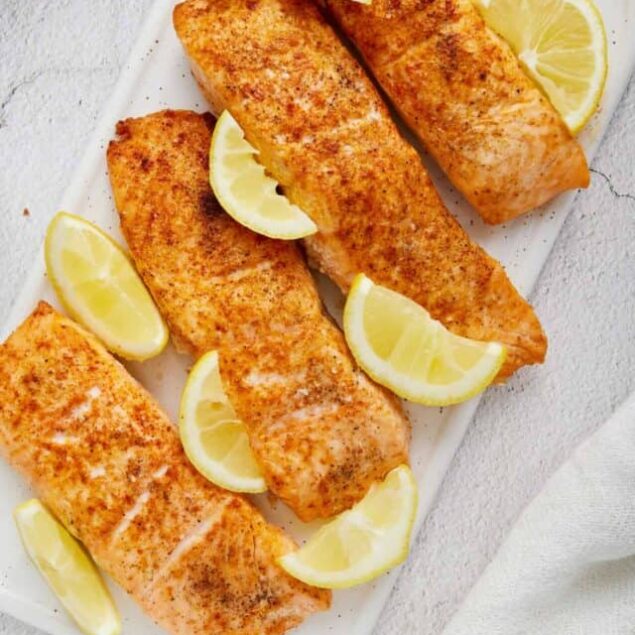Baked salmon fillets with lemon wedges on white platter, healthy seafood recipe.