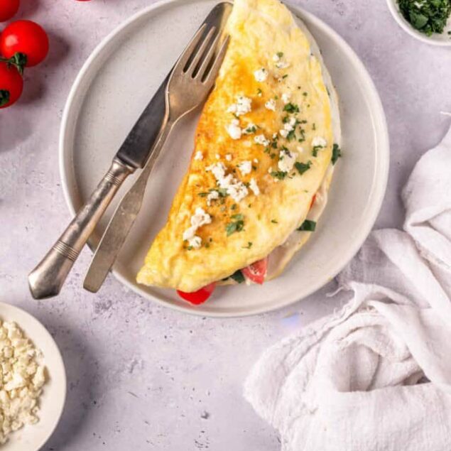 Scrambled eggs with herbs on a white plate with tomatoes and garnishes.