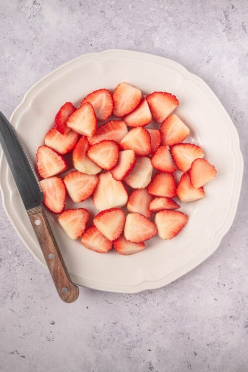Freshly sliced strawberries on a white decorative plate for baking or desserts.