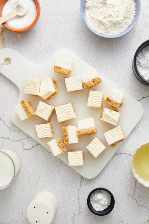 Buttercream frosted shortbread cookie bars on a white serving board, surrounded by baking ingredients, horizontal shot, clean aesthetic.