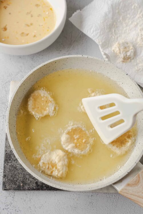 Fried chicken cooking in hot oil in a skillet with a spatula, close-up shot.