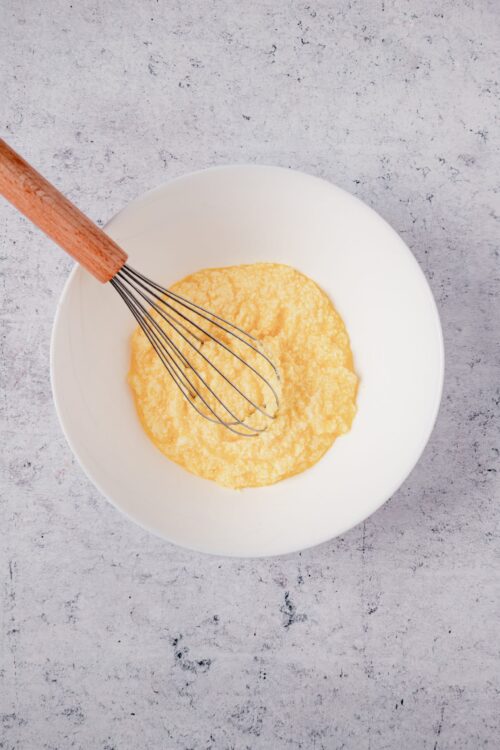 Fluffy yellow cake batter in a white mixing bowl with a whisk, ready for baking.