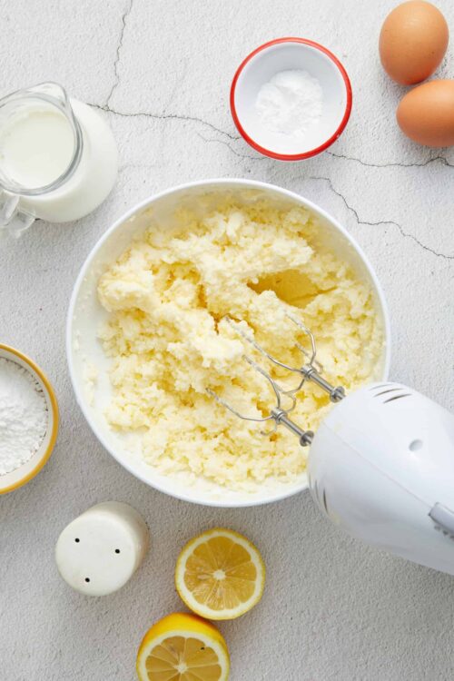 Fluffy lemon ricotta muffin batter in a large mixing bowl. Ingredients include flour, eggs, milk, and lemon slices.