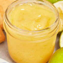 Lemon curd in a glass jar with fresh lemons and limes in the background.