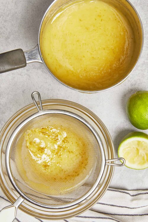 Lemon curd being strained through a fine mesh sieve for a smooth texture.