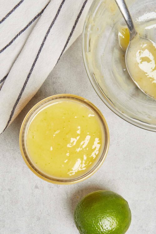 Lemon simple syrup in glass bowls on a light surface with a whole lime and striped cloth.
