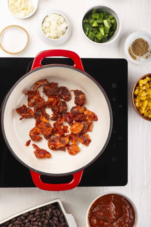 Cooked chorizo sausage in a red skillet on a black stovetop.