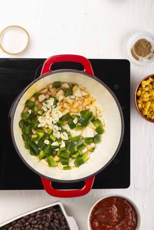 Sautéed green peppers, onions, and garlic in a red Dutch oven for a flavorful recipe.