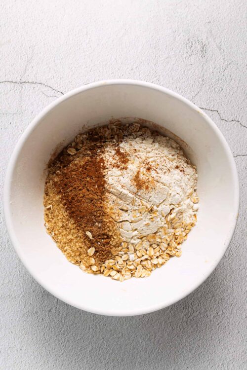 Cream, oats, and spices in a white mixing bowl for baking recipes.