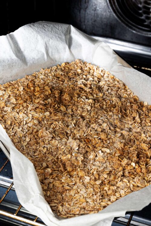 Crunchy homemade granola baking tray with oats and nuts in oven.
