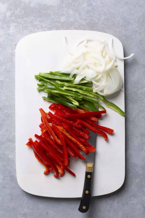 Sliced colorful bell peppers and onions on a white cutting board for healthy cooking.